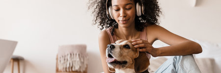 Young african woman in casual wear with beagle puppy at home, sitting on a floor, playing with dogの写真素材