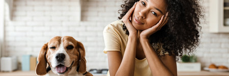 Smiling young african woman leaning on a kitchen counter with her pet beagleの写真素材