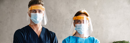 Two doctors wearing protective medical uniform standing in the cabinet, arms folded