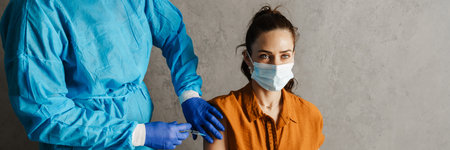 Woman patient wearing protective mask getting vaccinated from covid 19 by the doctor in his cabinetの写真素材