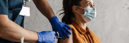 Sick woman in medical mask getting a vaccine shot sitting in a cabinet
