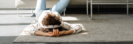 Young curly woman listening music with headphones while lying on floor at home