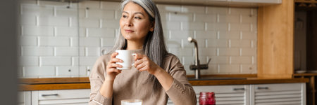 Mature grey woman drinking coffee while having breakfast in kitchen at homeの写真素材