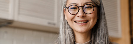Mature grey woman smiling while working with laptop in kitchen at home