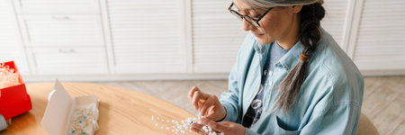 Mature grey woman in eyeglasses wrapping present at homeの写真素材