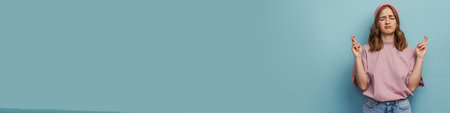 Young unhappy woman frowning and keeping fingers crossed isolated over blue background