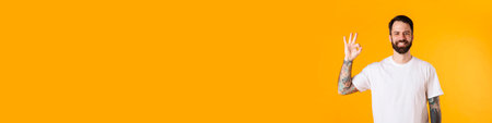 Portrait of a happy brunette bearded man standing over yellow wall, showing ok