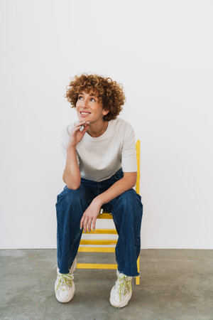 Ginger curly woman wearing t-shirt smiling while sitting on chair isolated over white backgroundの写真素材
