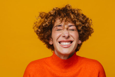 Excited ginger mature woman smiling with her eyes closed isolated over yellow studio backgroundの写真素材