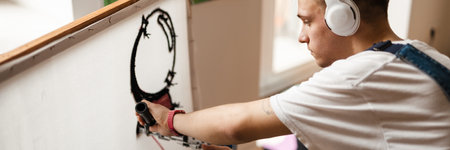 Young white man in headphones working on craft rug with sewing machine at homeの写真素材