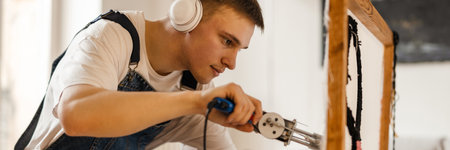 Young white man in headphones working on craft rug with sewing machine at home