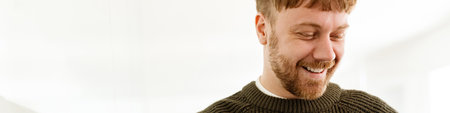 Young ginger man smiling and working with laptop while standing in office