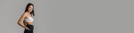 Smiling young white woman with long brunette hair wearing crop top standing posing over gray background side viewの写真素材