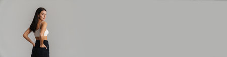 Young white woman with long brunette hair wearing crop top standing posing over gray background back viewの写真素材