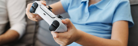 Close up cropped image of a little son with gamepad playing video game at home