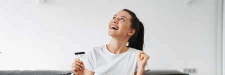 Excited woman making winner gesture while using credit card and laptop at home