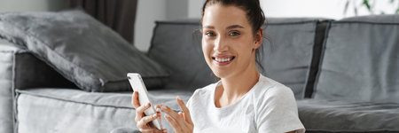 European smiling woman using mobile phone while sitting on floor at home