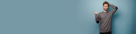 White ginger man with beard frowning and pointing finger aside isolated over blue background