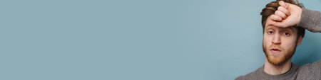 White ginger man looking at camera while wiping his forehead isolated over blue background