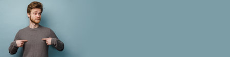 White ginger man with beard pointing fingers at himself isolated over blue background