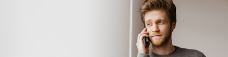 Ginger young man talking on mobile phone while standing indoors