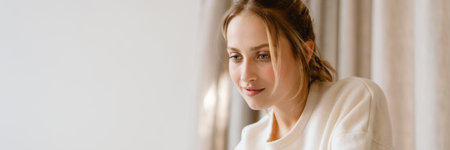 Young woman working with laptop and smiling in bedroom at homeの写真素材