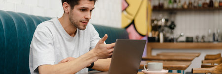 Confused young man student sitting in cafe indoors with laptop computer, studying or working