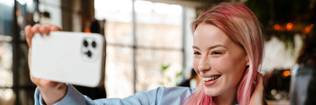 Young beautiful woman with pink hair taking selfie photo on cellphone while studying in cafe