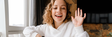 Young white woman gesturing and using laptop while sitting at table in homeの写真素材