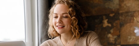 Young white woman writing down notes while working with laptop at home
