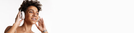 Young black woman listening music with headphones and smiling isolated over white backgroundの写真素材