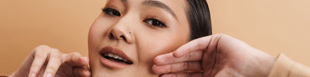 Young asian brunette woman posing and looking at camera isolated over beige background