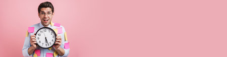 Young white man with stickers exclaiming while showing clock isolated over pink background