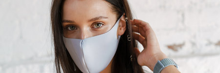 Young brunette white woman wearing protective medical mask standing over white wall background...