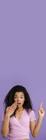 Young black woman pointing finger upward while expressing surprise isolated over purple backgroundの写真素材