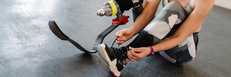 Young sportswoman with prosthesis tying her shoelaces while working out indoors