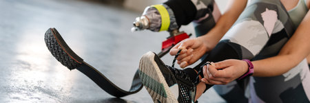 Young sportswoman with prosthesis tying her shoelaces while working out indoorsの写真素材