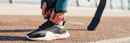 Cropped image of a young disabled woman with prosthetic lag tying shoelace outdoorsの写真素材