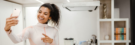 Black woman taking selfie on mobile phone while cooking in kitchen at home