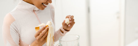 Black young woman smiling while making smoothie in kitchen at homeの写真素材