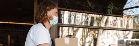 Young white cafe worker in face mask taking delivery outdoors