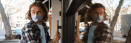 Young white cafe worker in face mask opening door outdoorsの写真素材