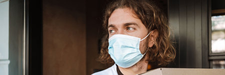 Young white cafe worker in face mask taking delivery outdoors