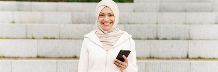 Middle eastern woman in hijab using mobile phone while working out outdoors