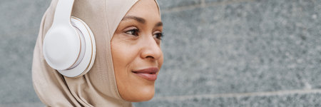 Middle eastern woman in hijab listening music with wireless headphones outdoors