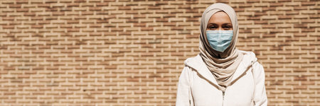 Middle eastern woman in face mask sitting on bench during workout outdoorsの写真素材