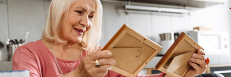 A smiling elderly woman looking at old photographs as part of sitting in the sunny kitchen