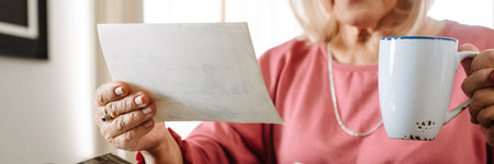 A close-up view of an elderly woman looking at old photos with a cup in her hands while sitting in a cafeの写真素材