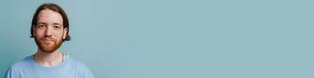Young ginger man with beard posing and looking at camera isolated over blue backgroundの写真素材