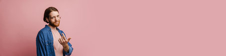 Young ginger man with beard looking at camera while calling and gesturing isolated over pink backgroundの写真素材